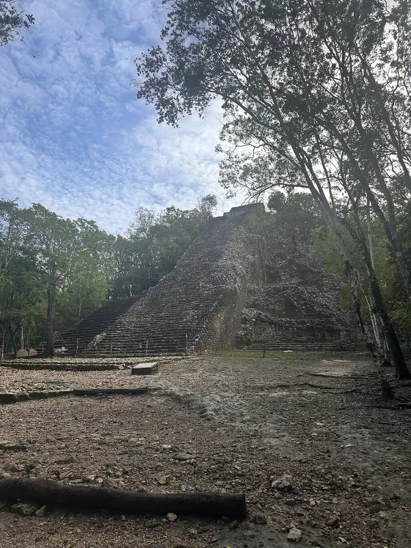 A path through dry forest at Coba with a stepped pyramid half hidden in the trees