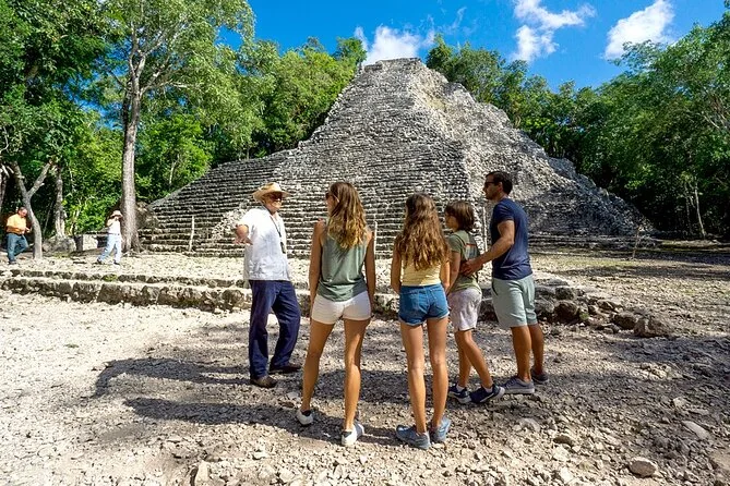 Four visitors with a guide standing at the foot of the Nohoch Mul pyramid in a clearing