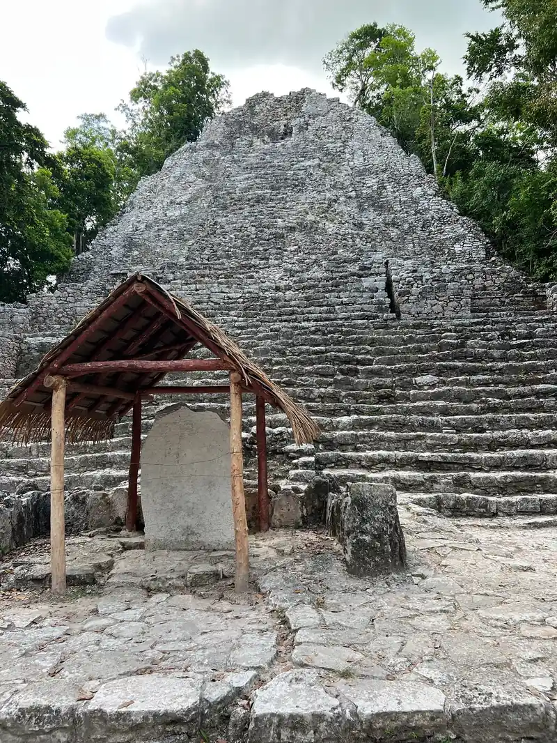 A Maya stepped pyramid with a thatched shelter in front, in the forest at Coba